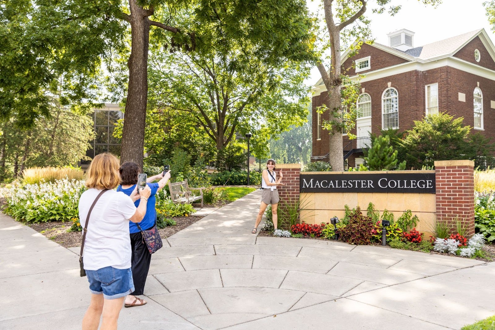 A Mac student poses in front of the Macalester College sign while friends take photos.