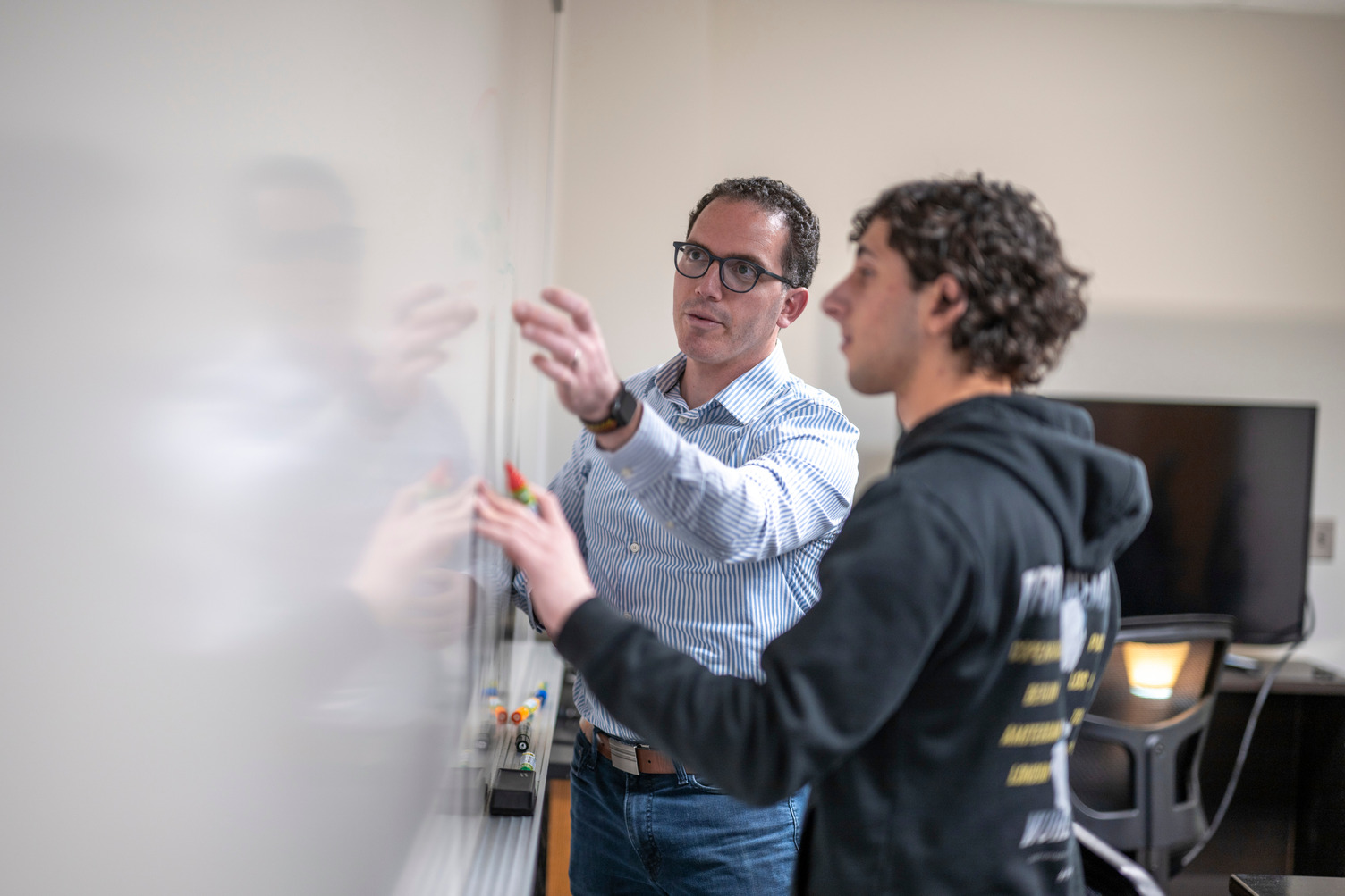 A professor and student work together at a whiteboard