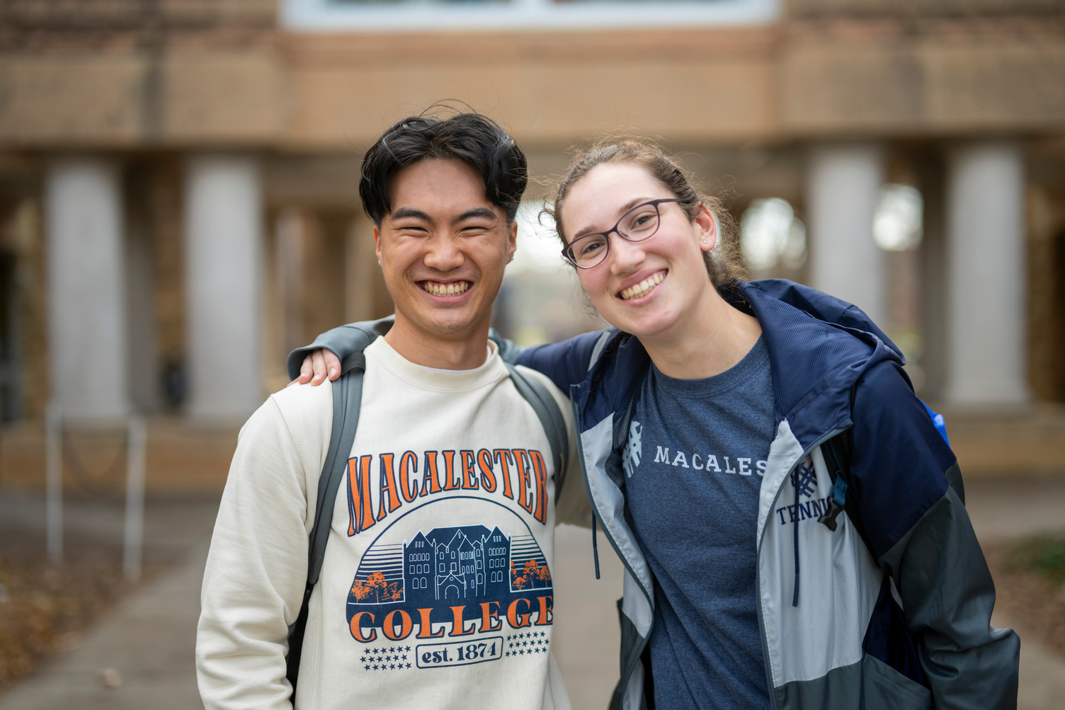 Two students pose together in front of the Library. They are wearing Macalester shirts.