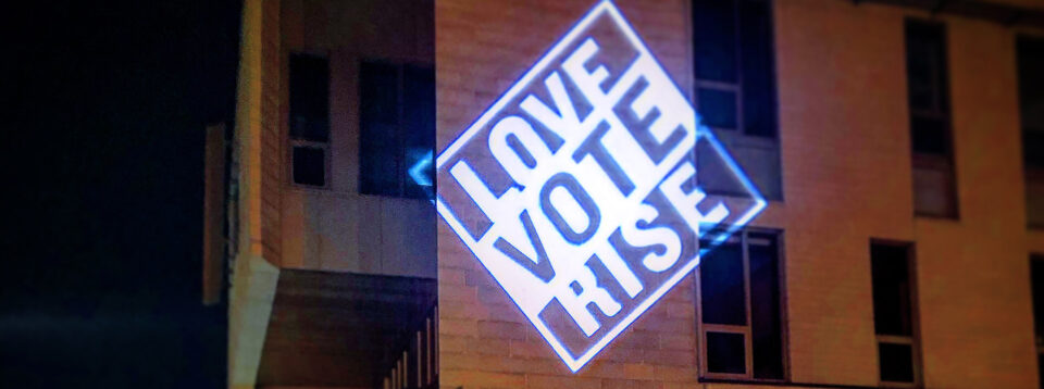 The text LOVE VOTE RISE projected on the wall of Markim Hall