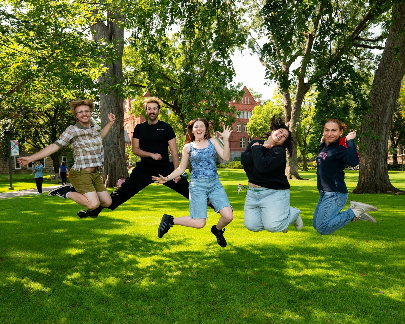 A group of students jumping in the air for a photo pose outside on the Macalester lawn.