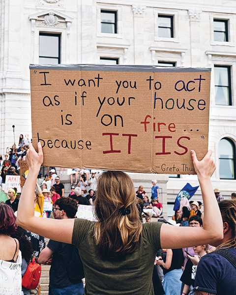 Photo of a Macalester student holding a sign reading "I want you to act as if your house is on fire... because IT IS - Greta Thunberg"