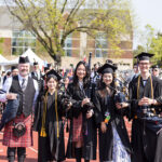 Director of Piping Mike Breidenbach poses for a picture with three students in graduation gowns and caps holding bagpipes