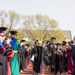 Two rows of students in graduation caps and gowns walk between two rows of professors in academic regalia