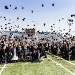 Class of 2024 graduates in graduation gowns toss their caps into the air