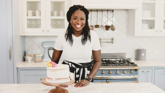 Zainab Mansaray-Storms ’09 poses with one of her cakes in a brightly-lit kitchen