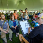 Two alumni pose for a portrait by a caricature artist