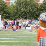 The Macalester mascot looks on as Reunion attendees on a football field participate in a water balloon sling shot contest