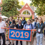 A group of five alumni stand behind a banner reading 2019