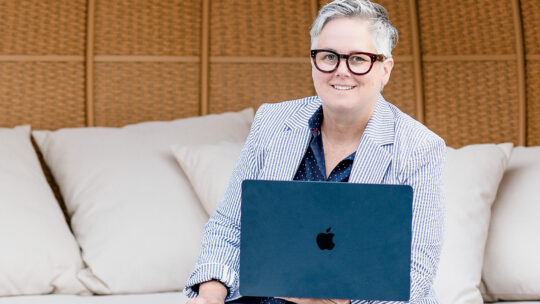 Erin DeRuggiero ’96 sits in an outdoor chair holding a laptop