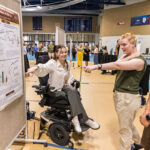 At the Summer Showcase, a student enthusiastically points to their research poster while two other students look on