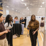 At the Summer Showcase, a student presents their research while looking at a poster as three others look on