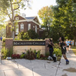 Macalester community members run past the Macalester College welcome sign at the Mac Fest 5k