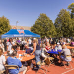 A line of people waits to receive hot dogs from a Macalester Athletics tent while others eat at tables on the Macalester track