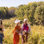 Three people stand in a field full of tall grass in the Ordway Natural History Study Area looking at clipboards