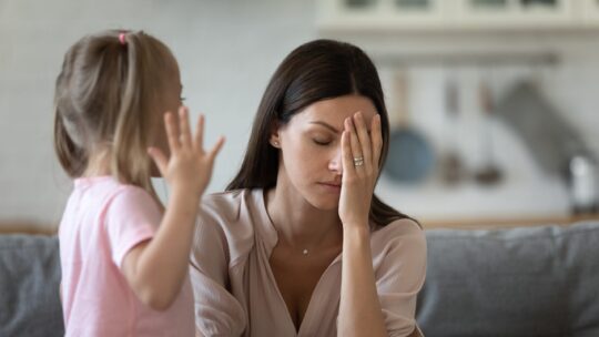 A mother holds her head in exasperation as her child gestures and speaks