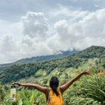 Student standing on a mountain overlooking a rainforest in Panama looks at the horizon with arms outstetched