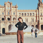 Student smiles in front of a fountain and historic building in Spain