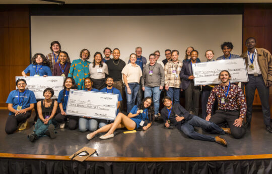 The three highest scoring Macathon teams pose together on stage at the final presentation, with their prize checks.