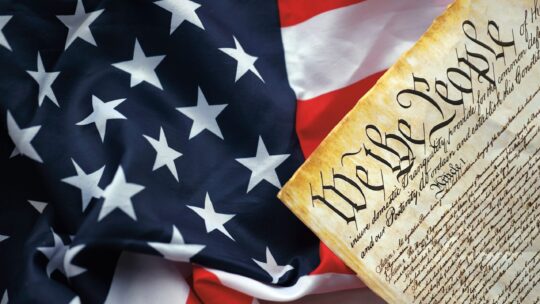 Stock image of the American flag with a copy of the Declaration of Independence in front of the flag.