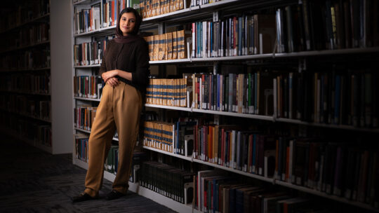 Professor Sarah Ghazal Ali standing in an aisle of books in a library