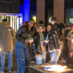 Three Mac students pose by a fire at the Brighter campaign launch event.