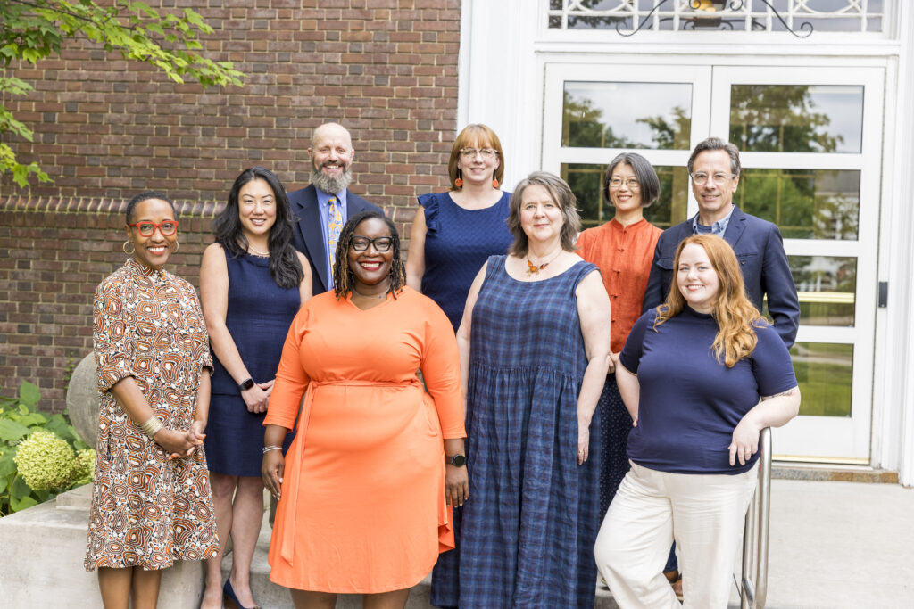 Nine members of the Provost's team pose on the steps in front of a brick building. They are all dressed in blue and orange.