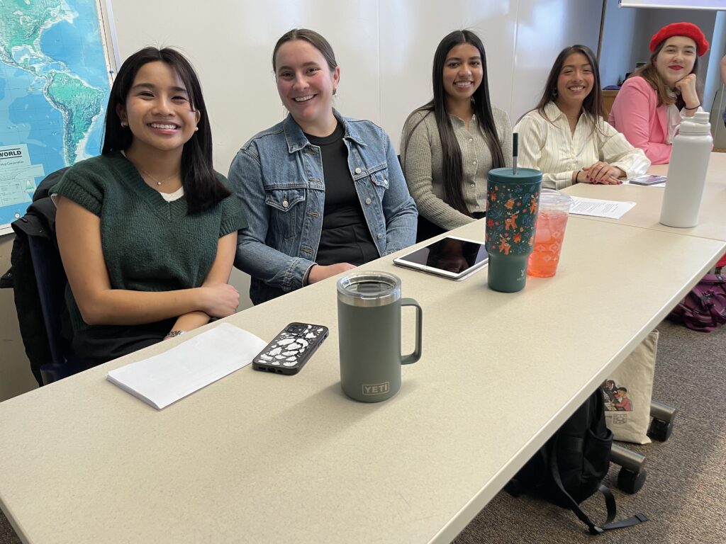 Sociology students sitting at a table and smiling as they think about "why"