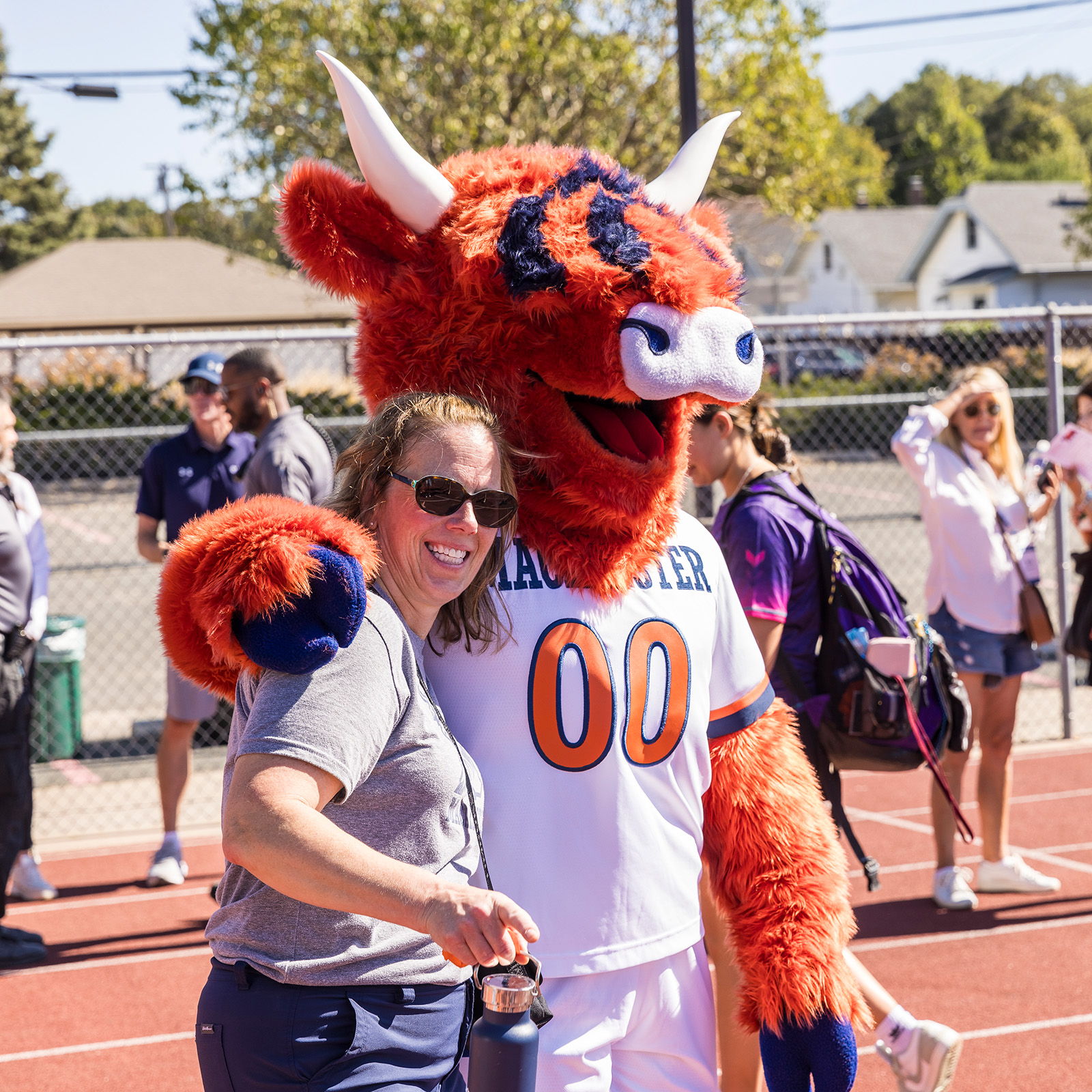 Coo the Highland Cow mascot hugs a community member as they pose for a photo.