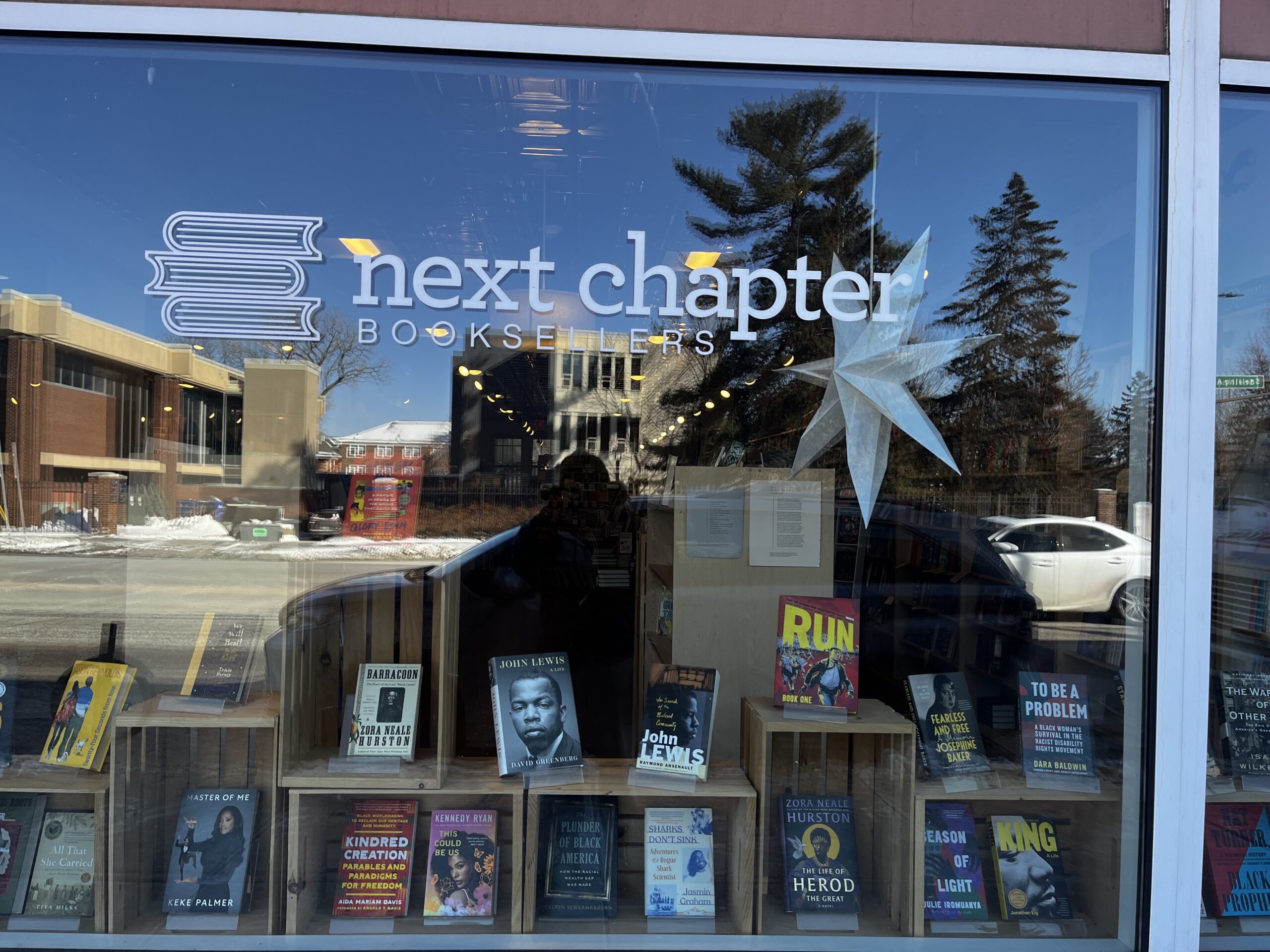 Next Chapter Bookseller storefront. The title of the store is on a glass window where books are displayed