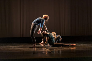 A seated dancer supports another as they lean backwards