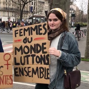 Elinor Jones holding cardboard sign reading "Femmes du monde luttons ensemble"