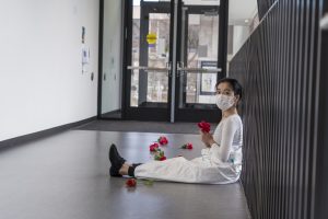 Performer sits in hallway surrounded by red flowers